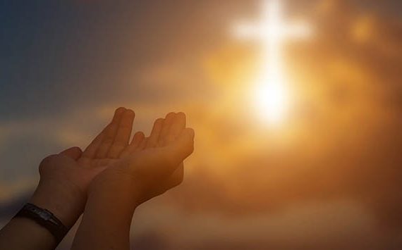 Hands lifted in worship with a glowing cross in the sky